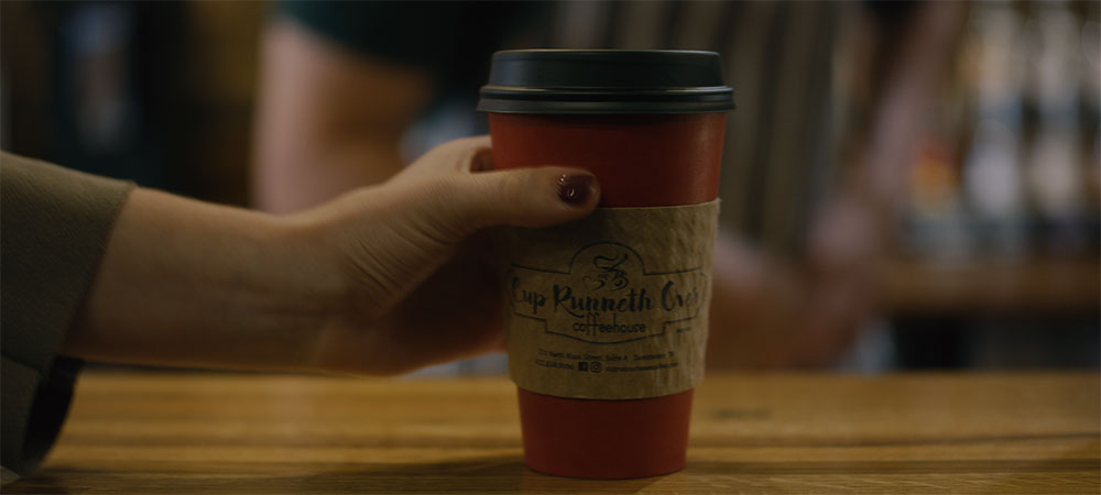 Hand holding a cup of coffee from Cup Runneth Over Coffeehouse